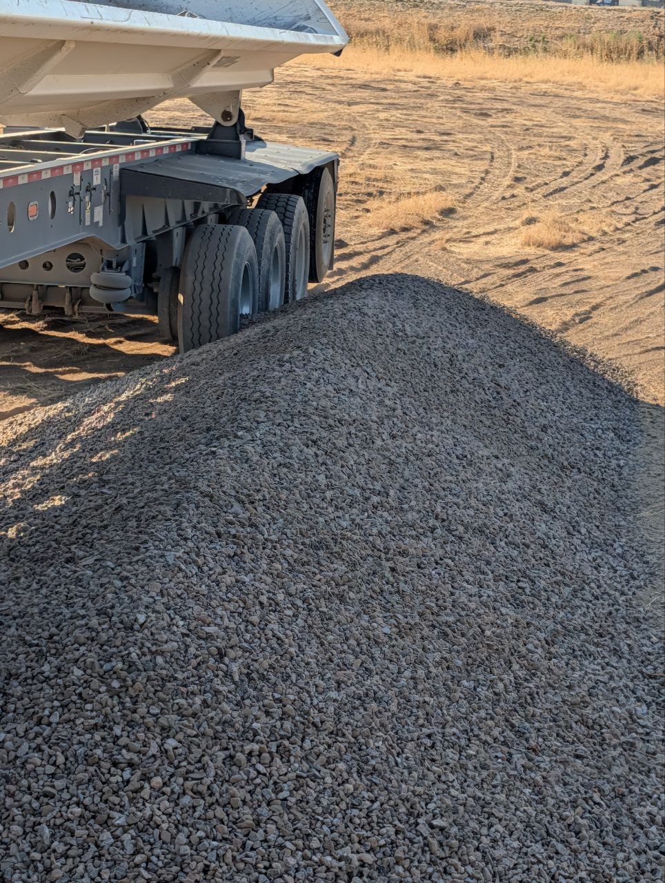 Freshly delivered pile of 3/4 gravel beside a side-dump trailer at a West Jordan, Utah jobsite.